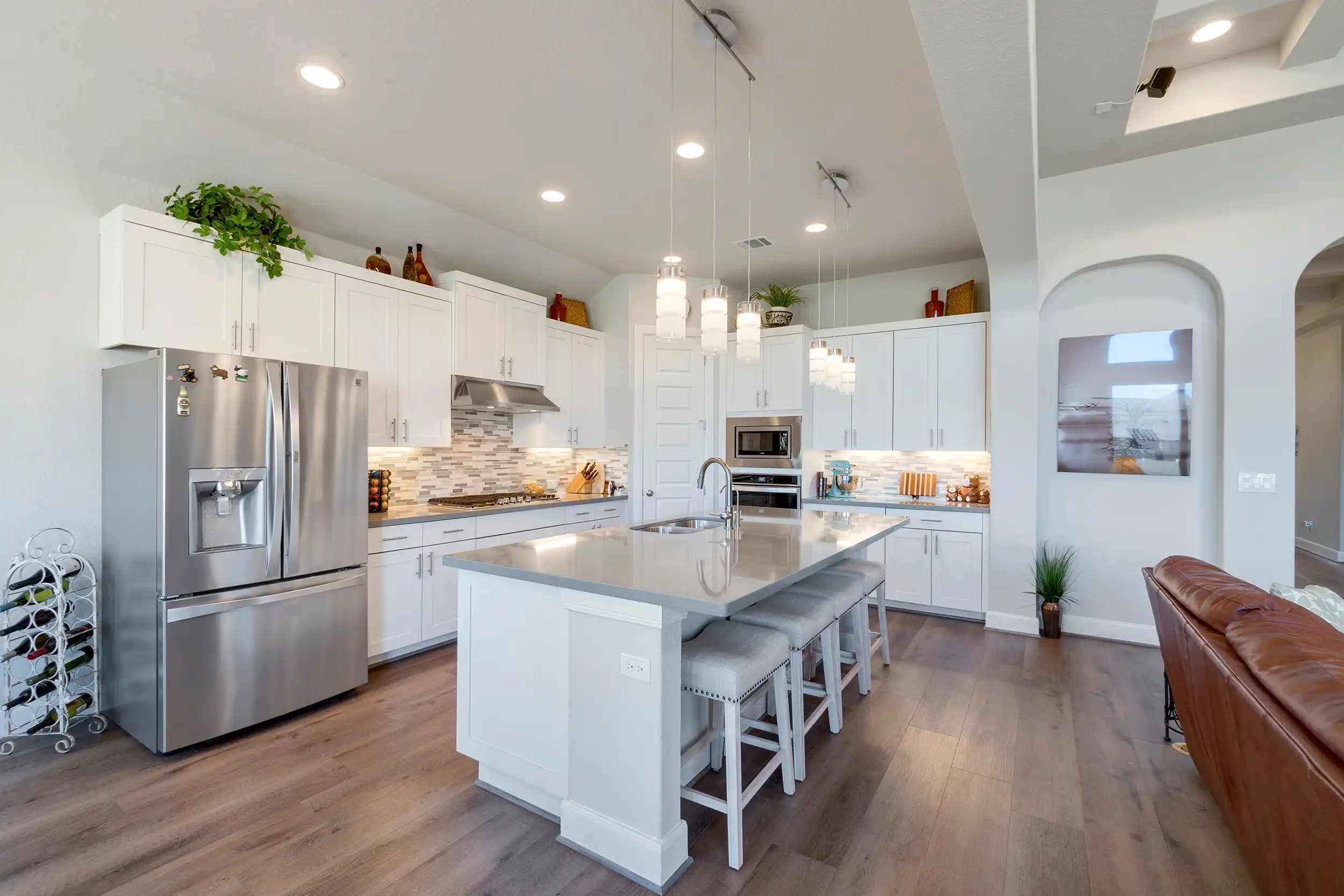 White kitchen with wooden flooring and silver American style fridge.